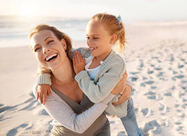 Cheerful mother playing with her daughter. Young woman having fun with her child on the beach. Little girl bonding on the beach with her mother. Happy parent on holiday with her child by the sea.