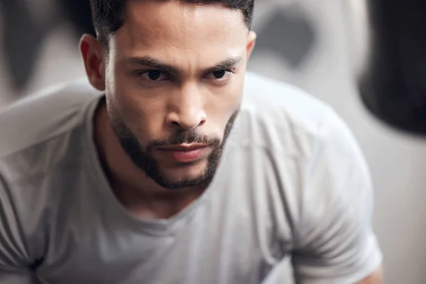 Closeup of one serious young hispanic man focused on his exercise session in a gym. Face of a determined mixed race guy getting mentally prepared to stay motivated and dedicated during a training wor.