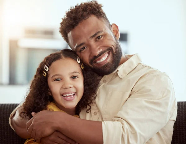 Portrait of mixed race single father and daughter hugging in home living room. Smiling hispanic girl embracing and bonding with single parent in lounge. Happy man and child sitting together on weeken.