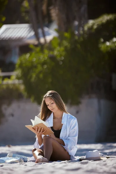 One beautiful young caucasian woman relaxing on the beach. Enjoying a summer vacation or holiday outdoors during summer. Taking time off and getting away from it all. Reading alone on the sand outsid.