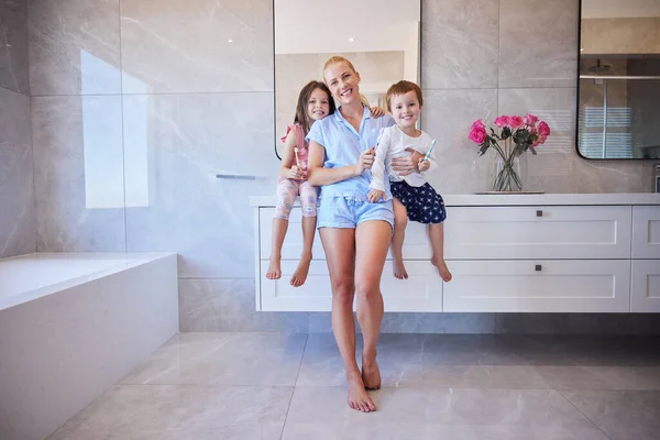 Happy young caucasian family holding toothbrushes and smiling showing off their healthy teeth. Young mother and her two children getting ready in the morning and brushing their teeth.