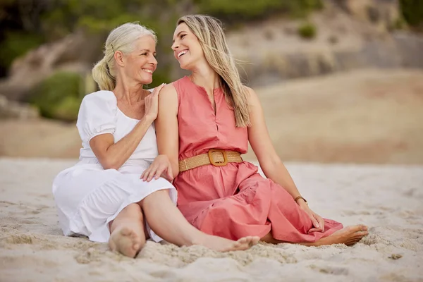 Closeup of a senior caucasian woman smiling and spending time with her daughter on vacation at the beach while sitting on the sand.
