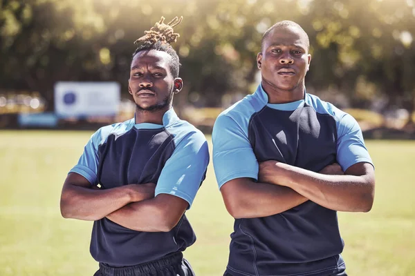 Portrait two young african american rugby players standing with their arms crossed outside on the field. Black men looking confident and ready for the match. Athletic sportsmen focused on the game.