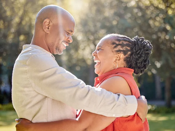 Happy affectionate mature african american couple sharing an intimate moment outside at the park during summer. In love seniors smiling and embracing while spending quality time together outdoors.