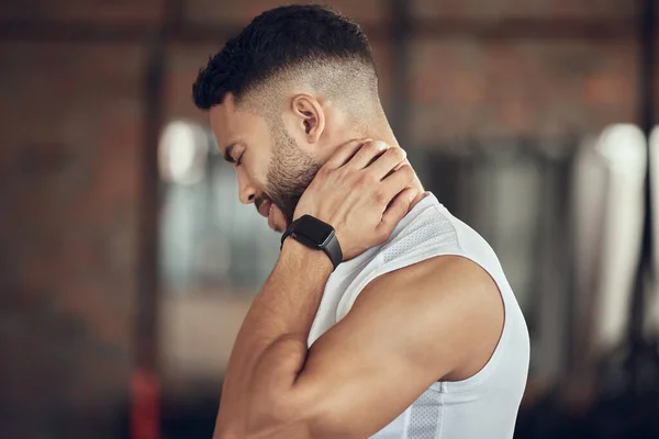 Young man with neck pain in the gym. Fit athlete with a stiff neck in the gym. Bodybuilder with a stiff neck in the gym. Active athlete with neck discomfort after a workout.