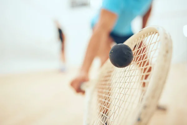 Closeup of unknown athletic squash player using a racket to hit a ball during a court game. Fit active mixed race male athlete training and playing in a sports centre. Healthy cardio and motion blur.