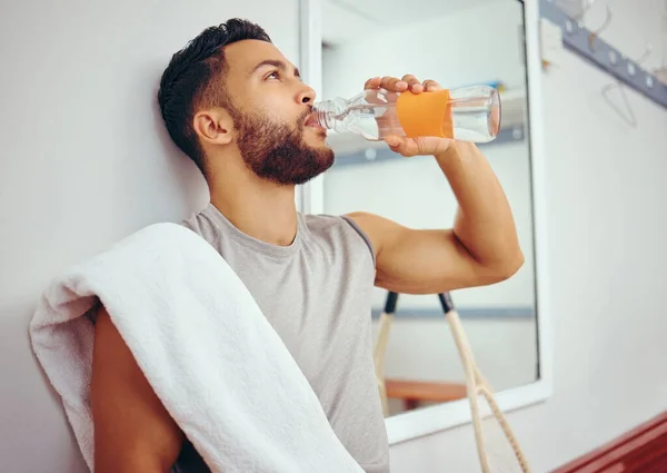 Hispanic player drinking water after his match. Young squash player relaxing after a match. Mixed race man sitting in a gym locker room drinking water. Water is needed after a match.