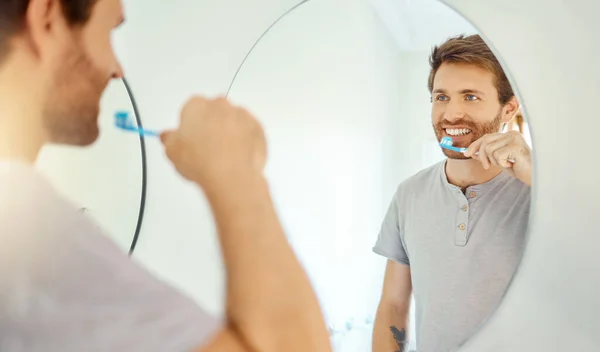 一个英俊的男人在家里的浴室里刷牙 白人男性使用美白牙膏 并对着公寓里的镜子看 — 图库照片