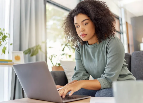 Young mixed race woman working on filling out forms while typing on a laptop at home. One focused hispanic female planning and sending an email alone in the lounge at home.