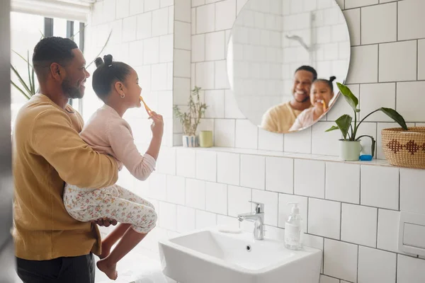 Happy mixed race father and daughter brushing their teeth together in a bathroom at home. Single African American parent teaching his daughter to protect her teeth.