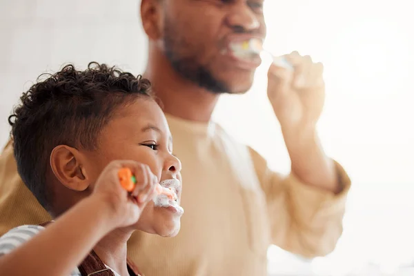 Happy mixed race father and son brushing their teeth together in a bathroom at home. Single African American parent teaching his son to protect his teeth.