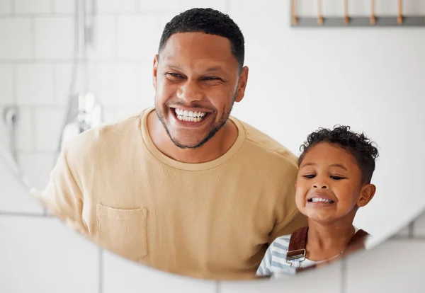 Happy mixed race father and son brushing their teeth together in a bathroom at home. Single African American parent teaching his son to protect his teeth.