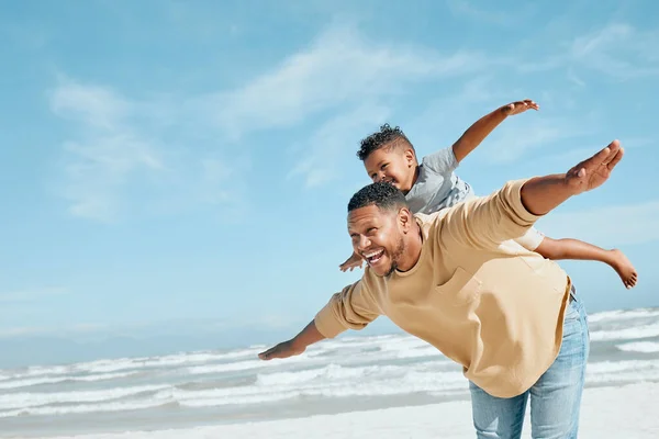Cheerful young mixed race father being playful while giving his son a piggyback ride on his back and stretching out their arms pretending to fly. Energetic dad and little boy having fun and spending .
