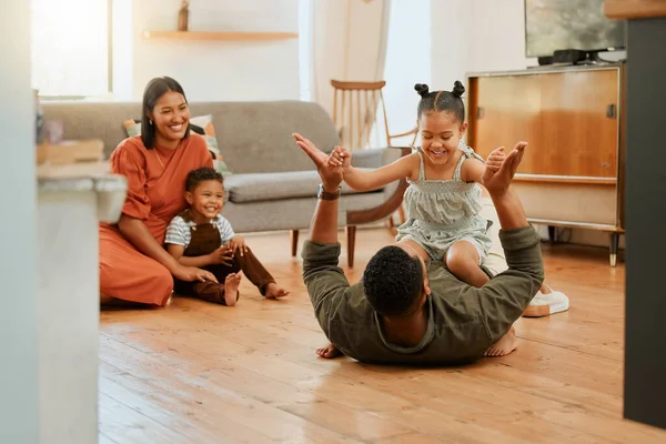 A happy mixed race family of four relaxing in the lounge and being playful together. Loving black family bonding with their kids while playing fun games on the floor at home.