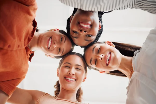 Portrait of happy businesswomen joining their heads together in a circle in an office at work. Diverse group of cheerful businesspeople having fun standing with their heads together in unity.