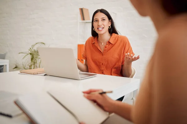 Young hispanic business woman using a laptop while speaking to colleagues during a meeting in an office boardroom. Staff sharing feedback and explaining ideas while brainstorming in a creative startu.