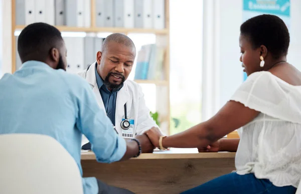 Couple in a consult with a doctor for ivf treatment. African american gp talking to a married couple. Young couple in fertility checkup with obstetrician. Caring prenatal doctor in hospital.