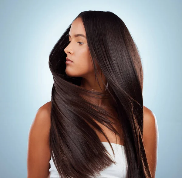 A hispanic brunette woman with long lush beautiful hair posing against a grey studio background. Mixed race female standing showing her beautiful healthy hair.