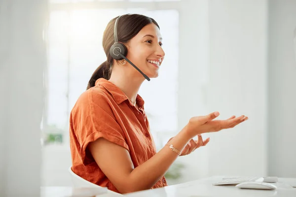 One happy young hispanic female call centre telemarketing agent talking on a headset while working on a computer in an office. Confident and friendly mixed race business woman consultant operating he.