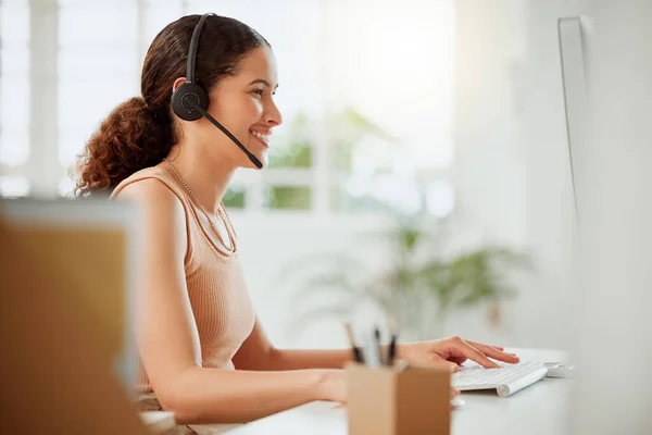 One happy young hispanic female call centre telemarketing agent talking on a headset while working on a computer in an office. Confident and friendly mixed race business woman consultant operating he.