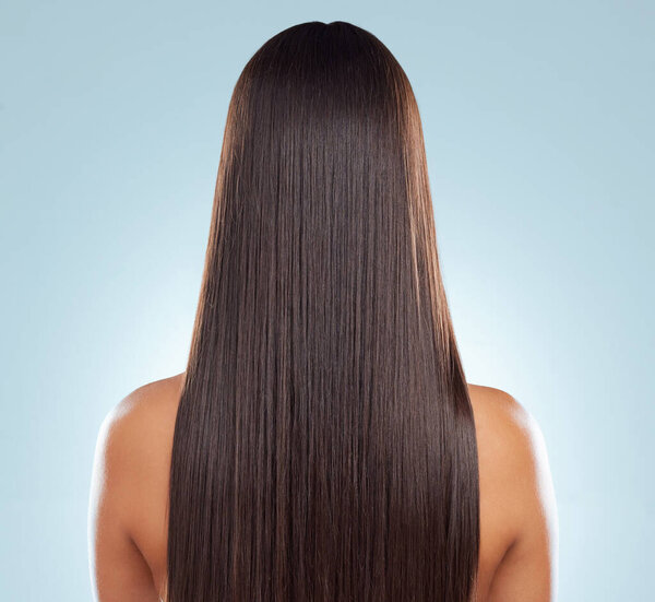 Rear view of a brunette woman with long lush beautiful hair posing against a grey studio background. Mixed race female standing showing her beautiful healthy hair.