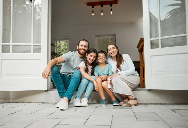4人の幸せな若い白人の家族が玄関のドアの笑顔でカメラを見て座っている 二人の両親は家の前で息子と娘と座っている — ストック写真