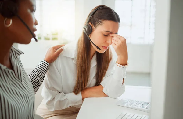 Stressed young hispanic call centre agent looking worried and suffering with headache while being comforted and consoled by a colleague in an office. Woman offering sympathy and support to frustrated.