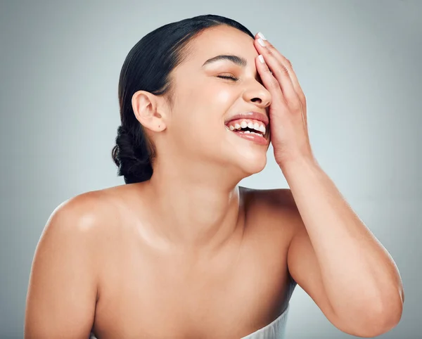 A beautiful young mixed race woman with glowing skin posing against grey copyspace background. Hispanic woman with natural looking eyelash extensions smiling while feeling her smooth skin in a studio.