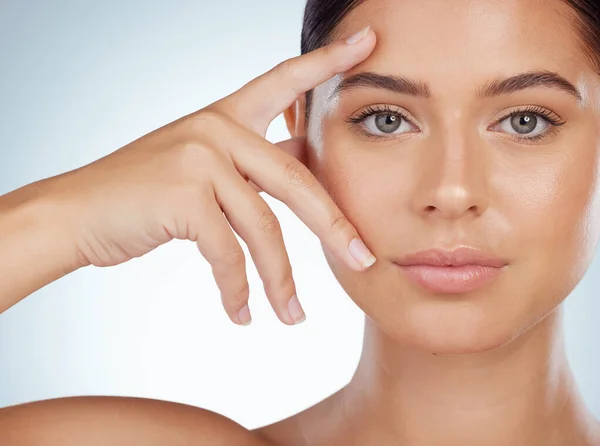 Closeup of beautiful woman with smooth glowing skin touching face in studio. Headshot of serious caucasian model isolated against grey background and showing manicured hand. Healthy self care routine.