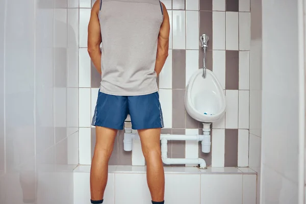 Back of a squash player urinating in his gym bathroom. Behind a fit man taking a break to urinate. Athletic man taking a break from his match to urinate in his gym toilet.