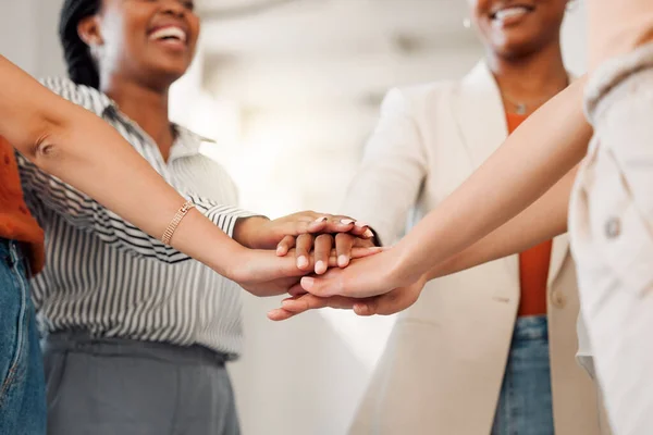 Group of businesswomen stacking their hands together in an office at work. Diverse group of businesspeople having fun standing with their hands stacked in unity.
