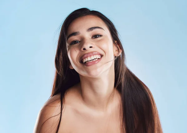 Portrait of one beautiful young hispanic woman with healthy skin and sleek long hair smiling against a blue studio background. Happy mixed race model with flawless complexion and natural beauty.