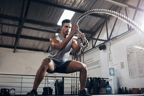 Health, gym and battle rope workout with man at a fitness center, cardio and muscle training. Power, energy and exercise by muscular athlete focused on intense movement, strength and endurance.