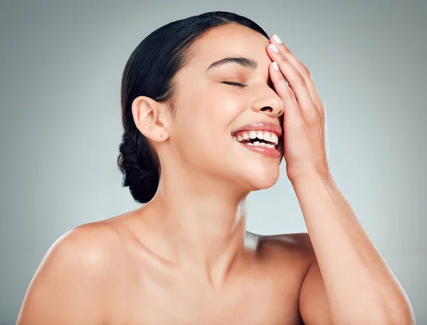 A beautiful young mixed race woman with glowing skin posing against grey copyspace background. Hispanic woman with natural looking eyelash extensions smiling while feeling her smooth skin in a studio.