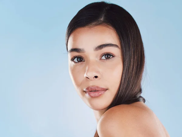 Portrait of one beautiful young hispanic woman with healthy skin and sleek hair posing against a blue studio background. Mixed race model with flawless complexion and natural beauty.