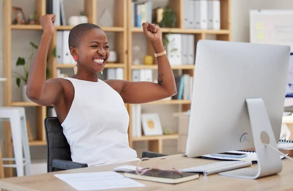 Excited cheerful african american businesswoman cheering for her success after reading an email on her computer. Lucky young business professional winning and celebrating good news in her office.
