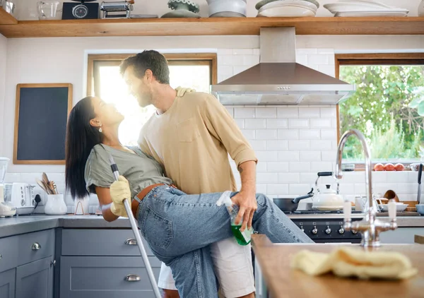 快乐的跨种族年轻夫妇一边跳舞一边一起打扫他们的家 年轻的高加索男人和惊慌失措的女人一边在厨房做家务活一边玩乐 — 图库照片