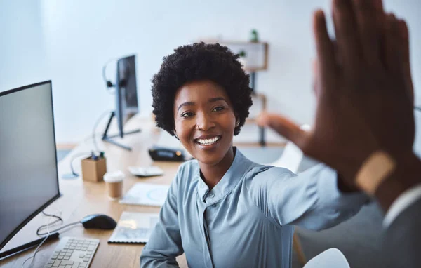 Happy african american call centre telemarketing agent giving colleague high five and cheering with joy while working in an office. Excited and ambitious female consultant celebrating successful sale.