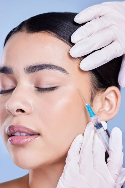 A gorgeous mixed race woman getting botox filler in her face. Hispanic model getting cosmetic surgery against a blue copyspace background.