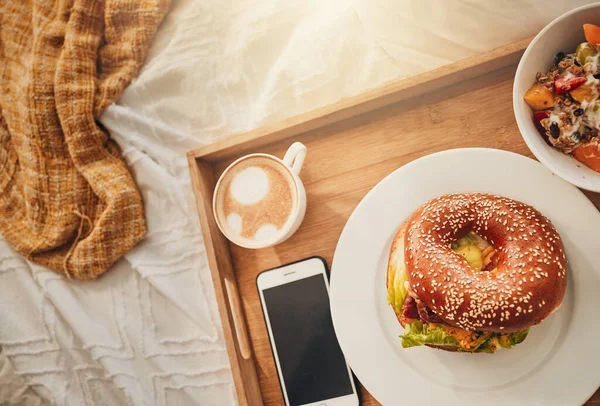 The perfect mothers day gift. A tray of a well balanced breakfast, a bagel, coffee and a cellphone. Everything needed for breakfast in bed.