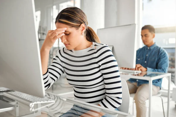 Young stressed mixed race businesswoman suffering from a headache while working on a desktop computer at work. One unhappy hispanic female businessperson suffering from anxiety while working on a com.