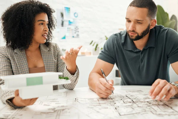 Two architectural coworkers planning a building project. Young designers working on a blueprint. Businesspeople collaborate on a building project. Professional designers working together on a 3D mode.