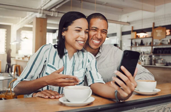 年轻的混血儿坐在餐桌边喝咖啡 一边在咖啡店里看智能手机里的东西 爱你的夫妻一边自拍一边笑 一边在手机上打电话 — 图库照片
