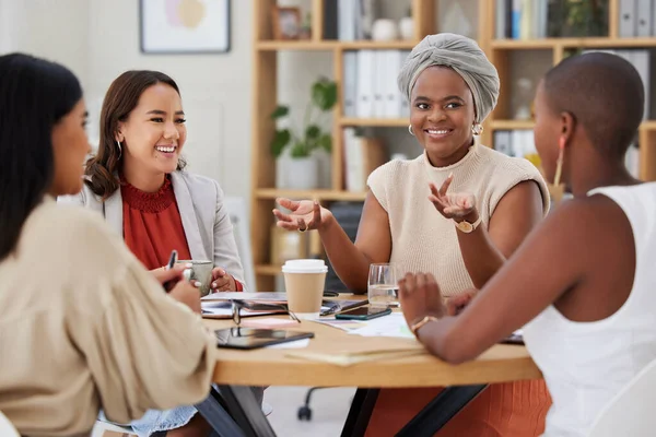 Diverse group of smiling business women having a brainstorm meeting in office. Happy confident professional team sitting together and using paperwork while talking and planning a marketing strategy.