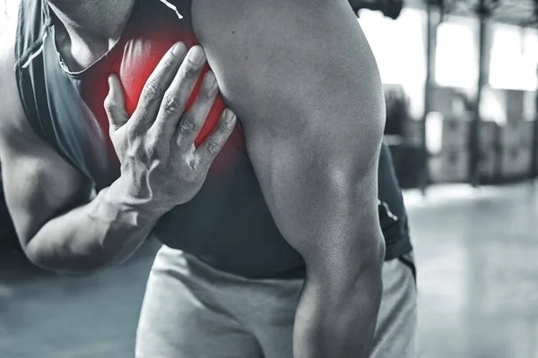 Is this a heart attack Trainer experiencing chest pains at the gym. Hand of a bodybuilder touching his chest in pain. Red CGI spots are used to show pain. Your heart may be in danger with exercise.