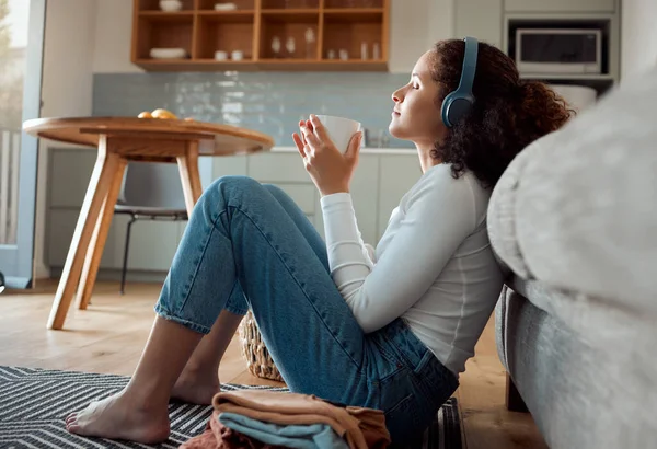 Woman enjoying a cup of tea. Young woman listening to music in her headphones drinking coffee. Hispanic woman drinking a cup of tea sitting on the floor. Woman relaxing, enjoying a beverage at home.