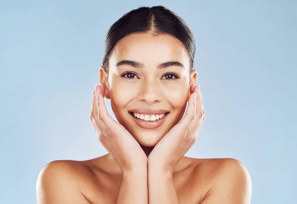 Closeup face beautiful young mixed race woman. Attractive female touching her face in studio isolated against a blue background. A skincare regime to keep your skin soft, smooth, glowing and healthy.