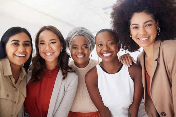 Portrait of a diverse group of smiling ethnic business women standing together in the office. Ambitious happy confident professional team of colleagues embracing while feeling supported and empowered.