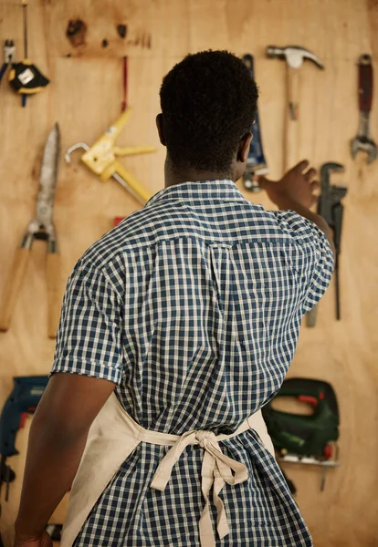 木匠从墙上捡工具的背面 非洲裔美国企业家决定一种工具 富有创意的商人从他的墙上挑选工具 卡彭特从他的收藏品中寻找工具 — 图库照片