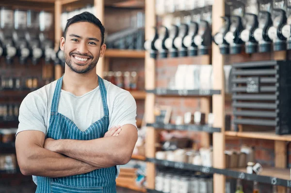 Portrait of one happy young hispanic waiter standing with his arms crossed in a store or cafe. Friendly man and coffeeshop owner managing a successful restaurant startup.